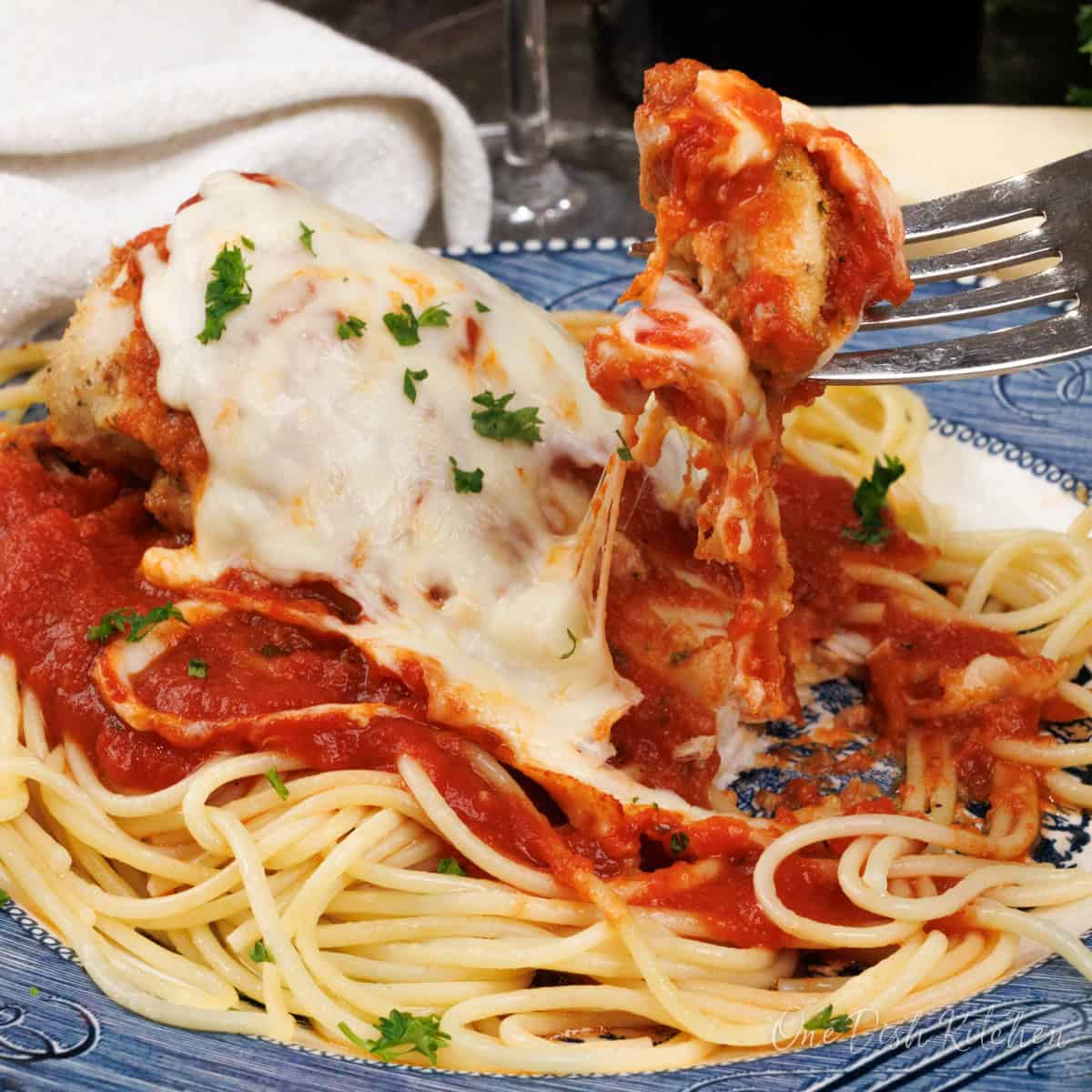 a fork holding a bite of chicken parmesan with melted cheese over a plate of pasta.