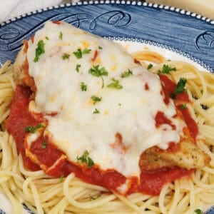 Chicken Parmesan topped with tomato sauce and melted mozzarella cheese on a blue plate.