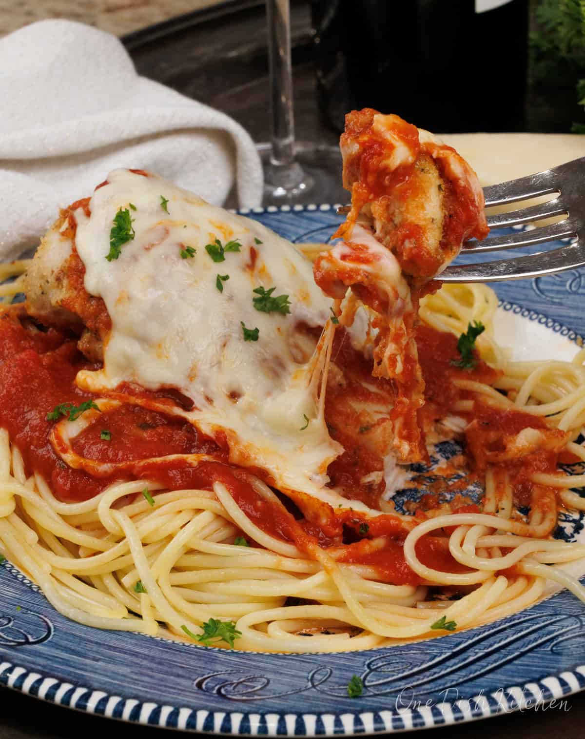 a fork holding a bite of chicken parmesan with melted cheese over a plate of pasta