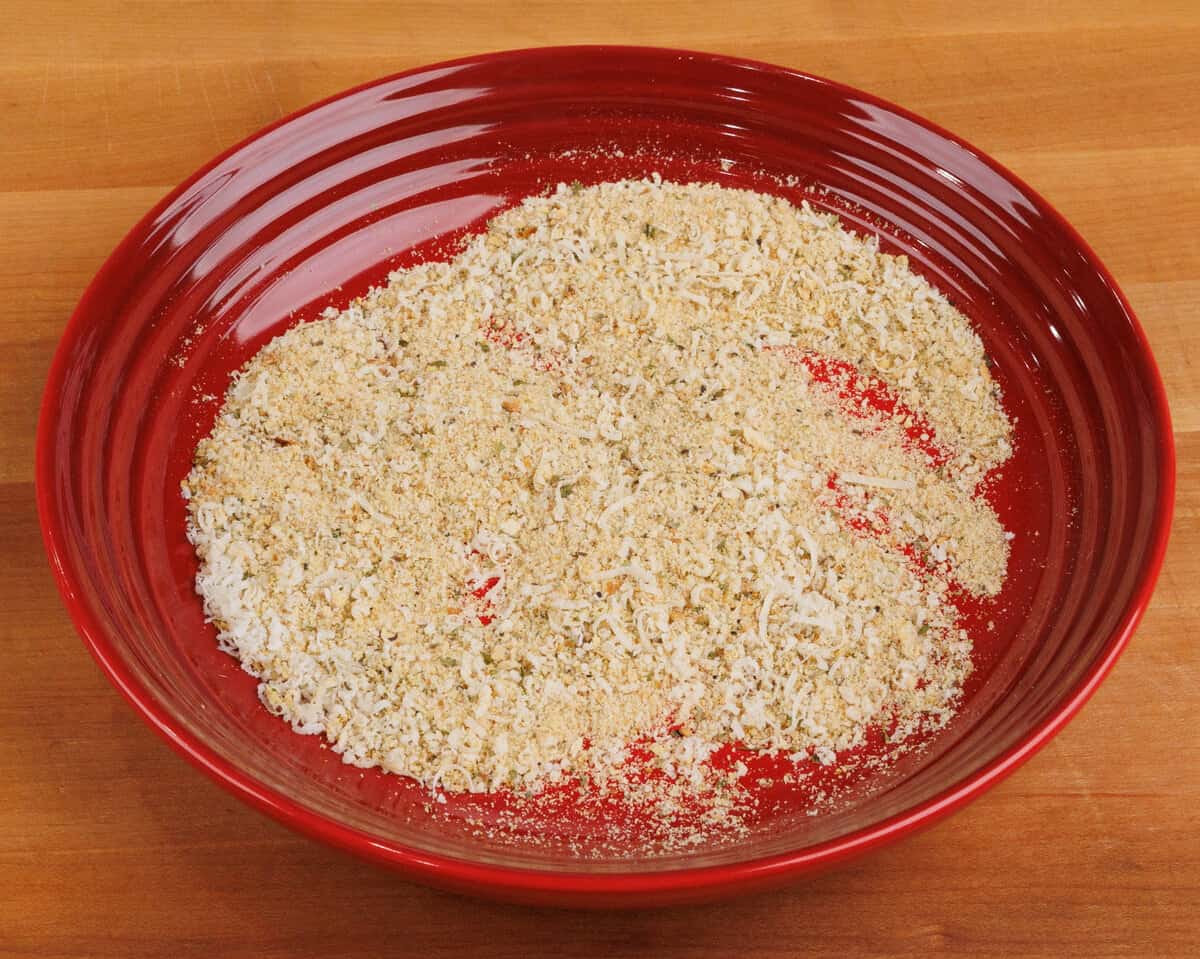 breadcrumbs and other seasonings in a red bowl on a kitchen counter.