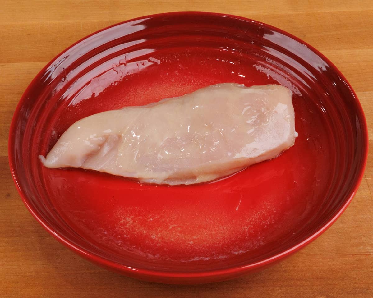 one raw chicken breast coated with melted butter in a red bowl