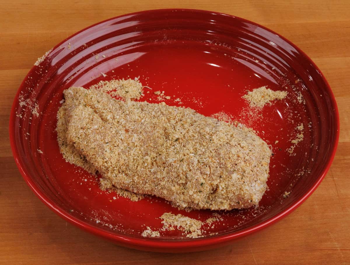a boneless, skinless chicken breast coated with bread crumbs in a red bowl