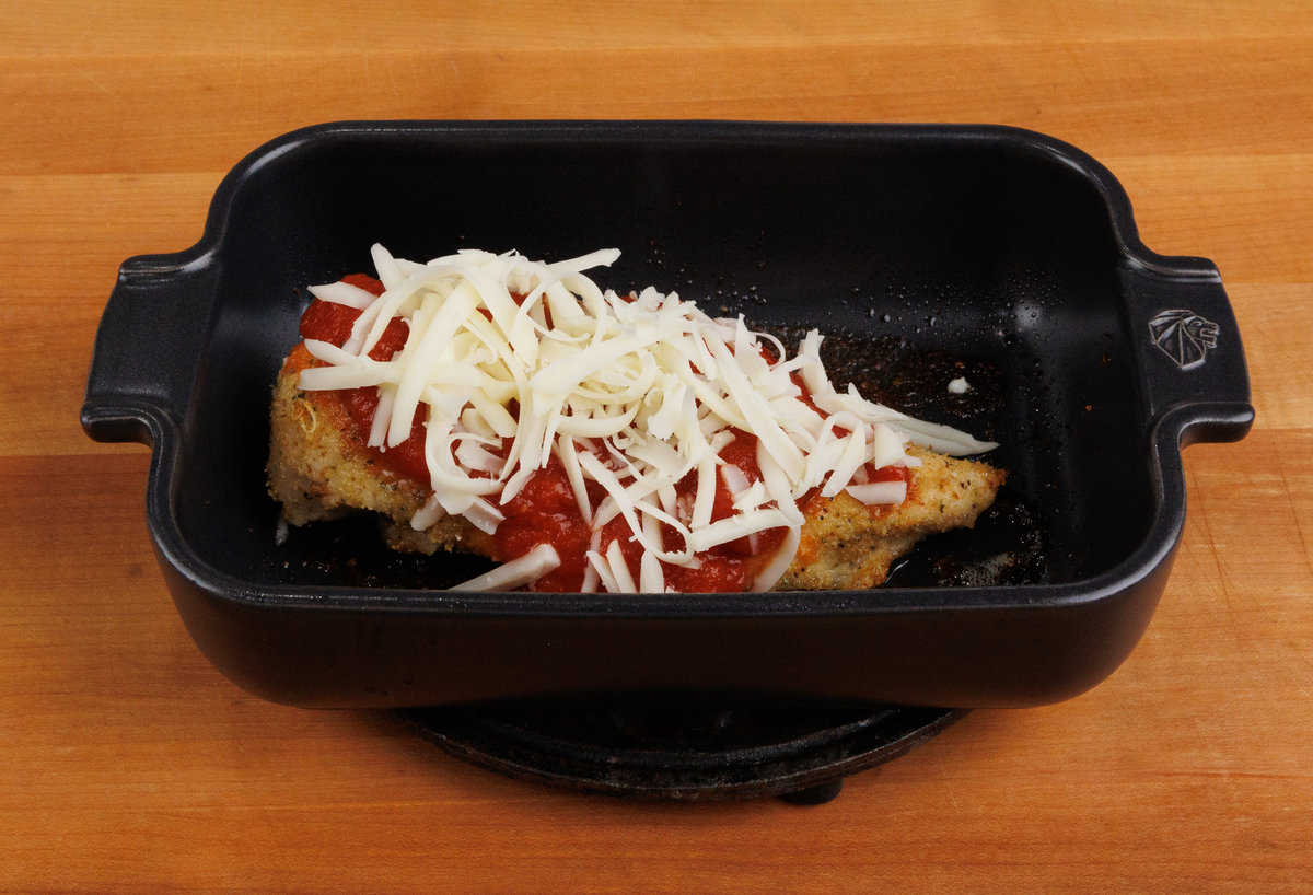 partially baked chicken parmesan in a dish topped with sauce and unmelted mozzarella cheese