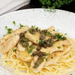 chicken piccata served over spaghetti on a white plate next to parsley and a white napkin