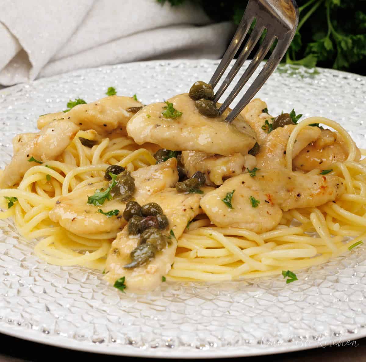 a forkful of chicken with pasta and piccata sauce over a plate