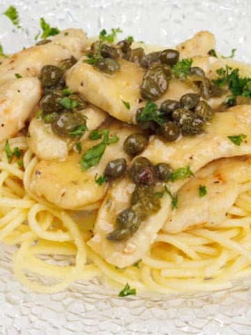 chicken piccata served over spaghetti on a white plate next to parsley and a white napkin
