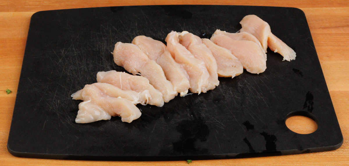 one chicken breast cut into ¼ inch strips on a black cutting board
