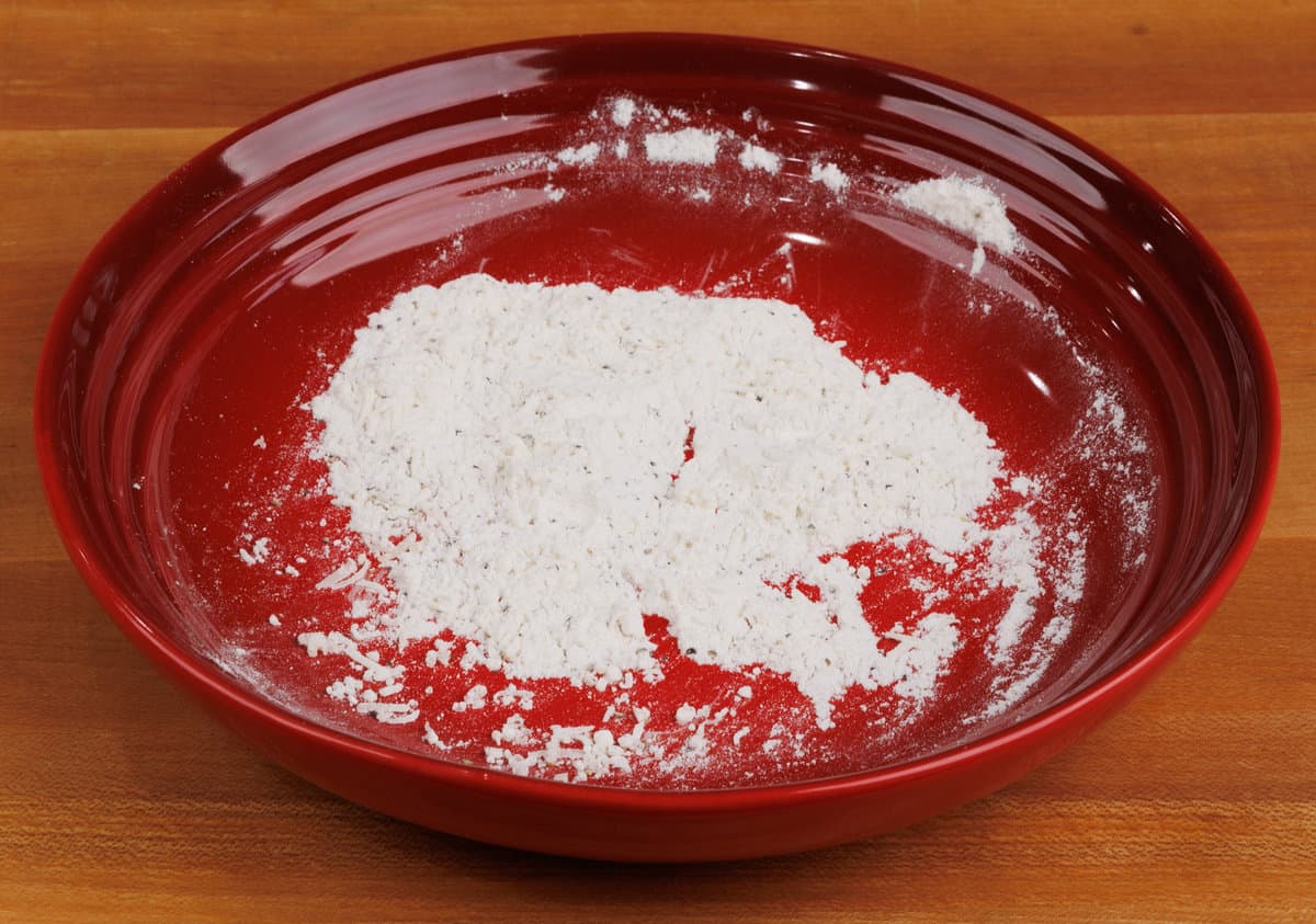 flour, salt, pepper, and parmesan cheese in a red bowl on a wooden counter