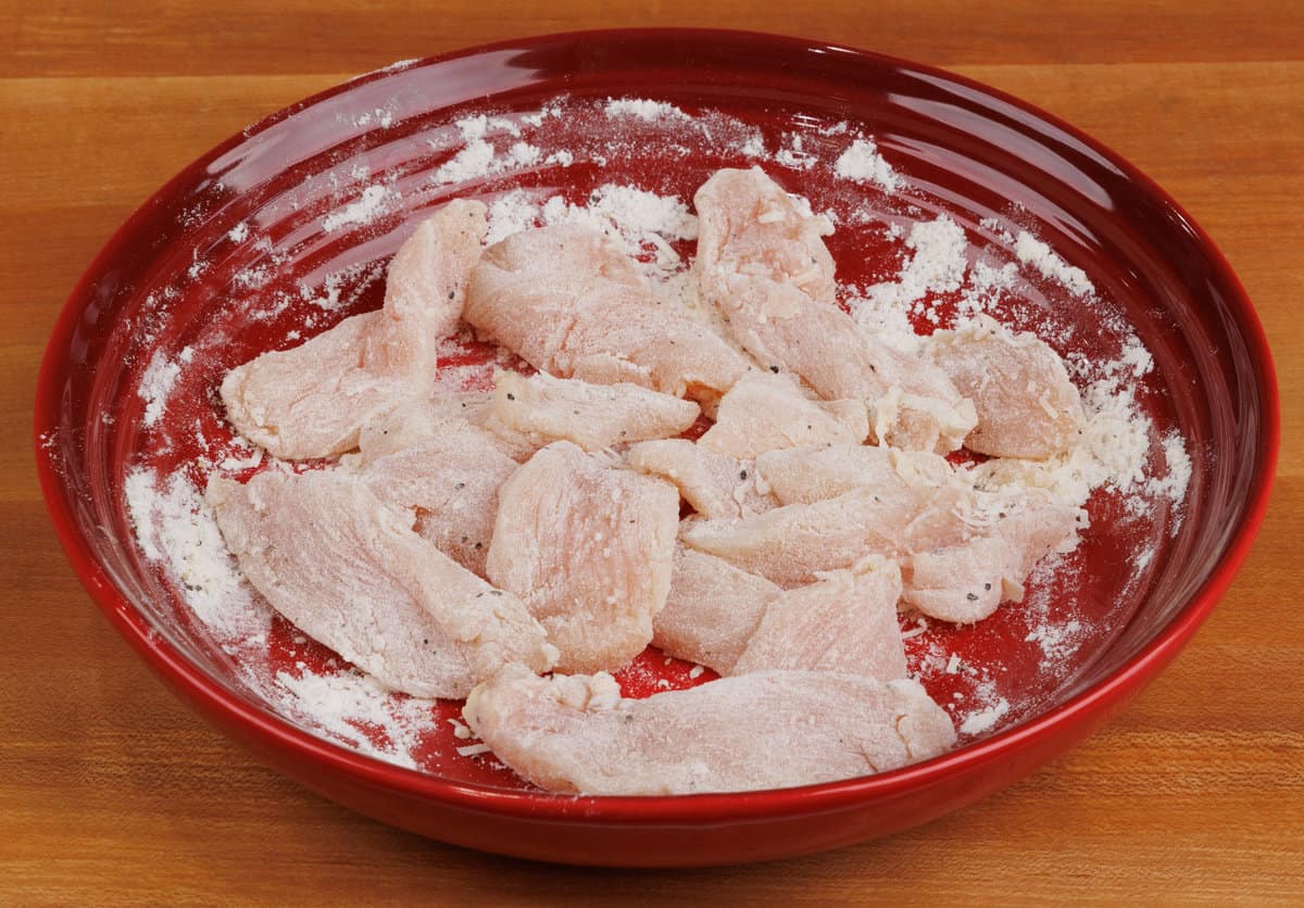 strips of chicken dredged in flour in a red bowl
