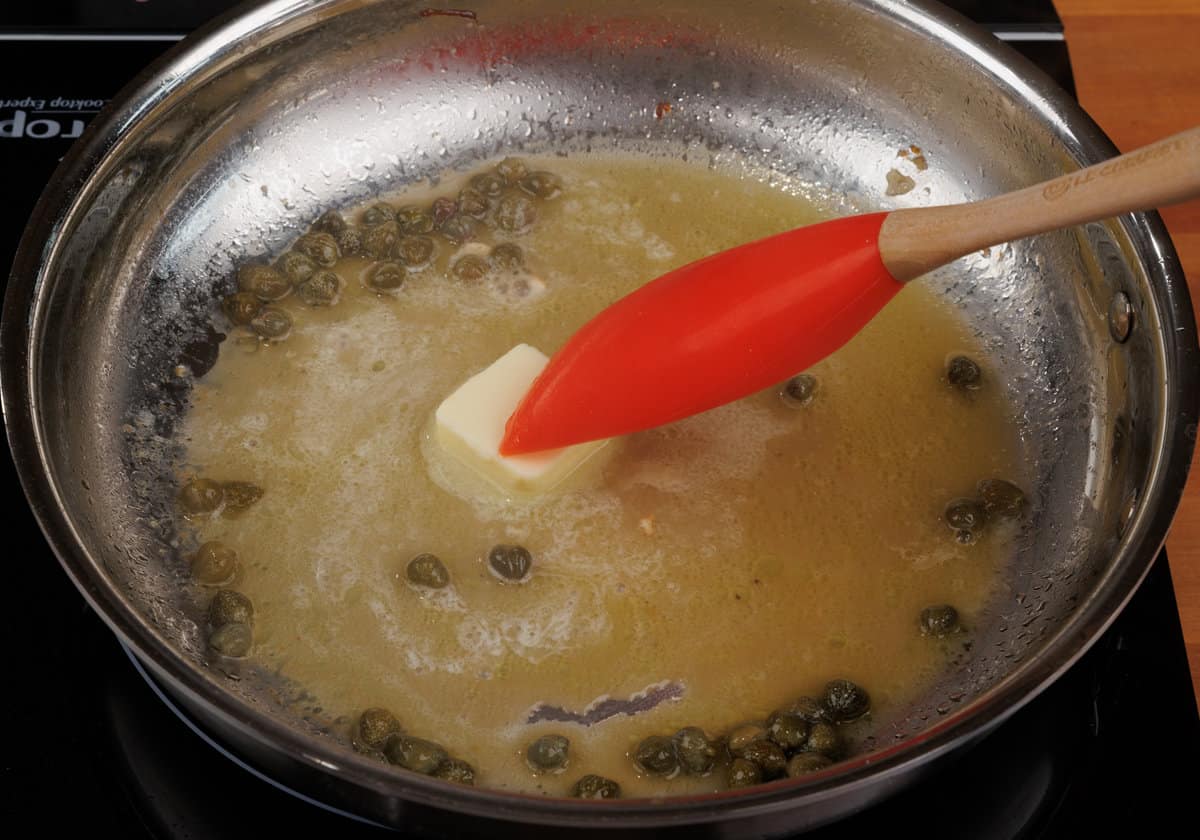 butter melting in chicken piccata sauce on the stove in a skillet