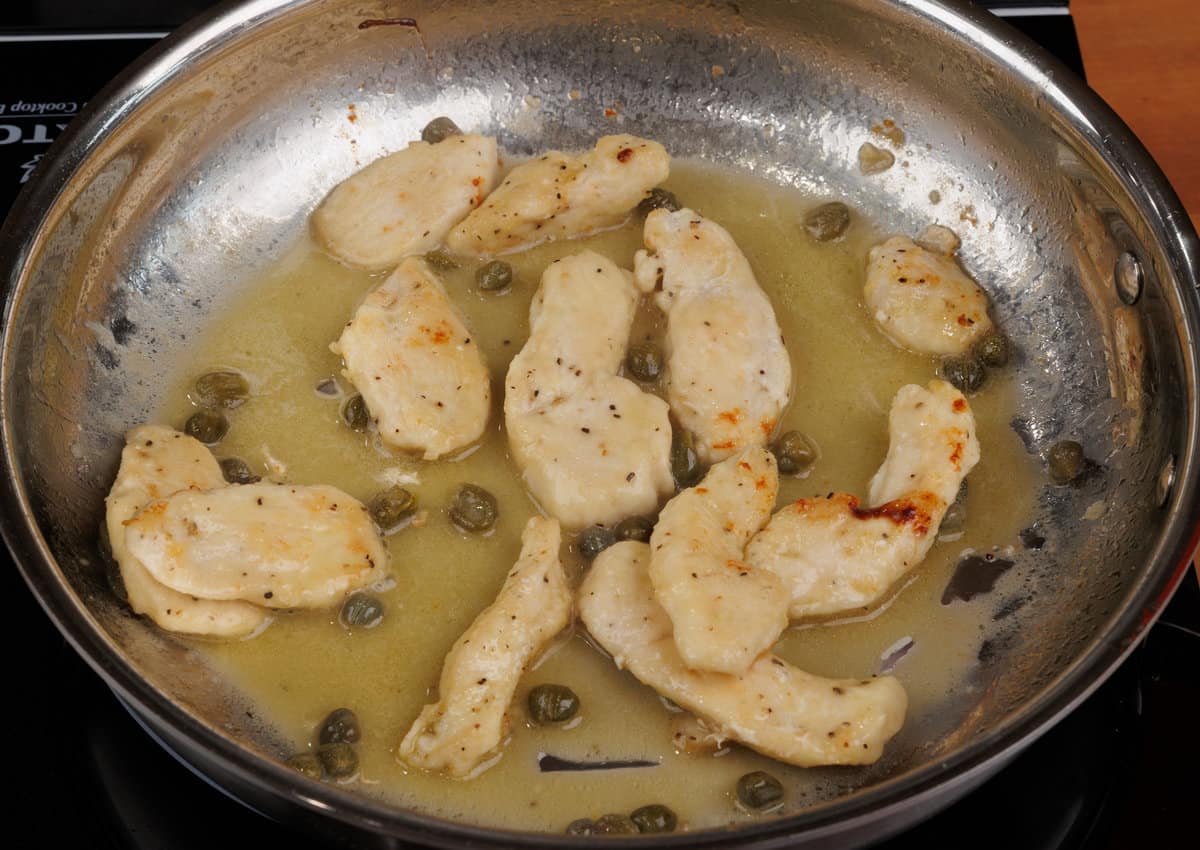 thin pieces of chicken simmering in a piccata sauce on the stove