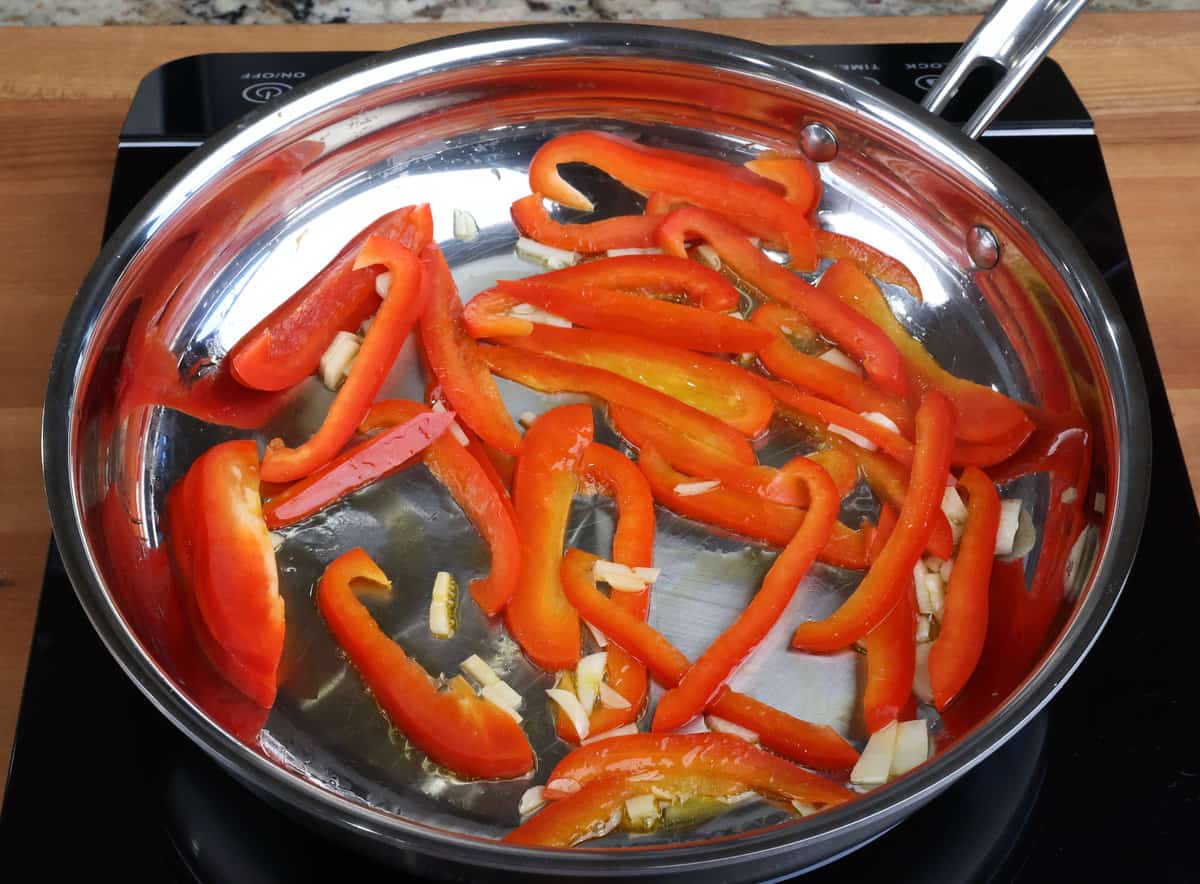 sliced red bell peppers and minced garlic cooking in a skillet