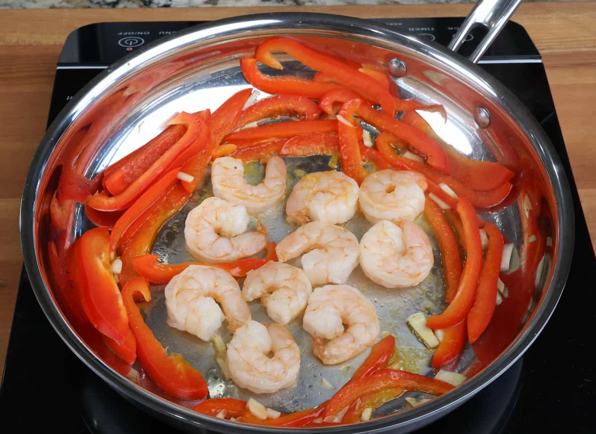shrimp cooking in a skillet alongside sliced peppers and garlic