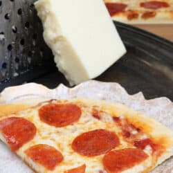 a slice of pepperoni pizza on a white plate next to a block of mozzarella cheese and a red napkin