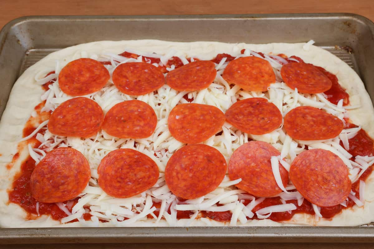 an unbaked pepperoni pizza on a rectangular baking sheet