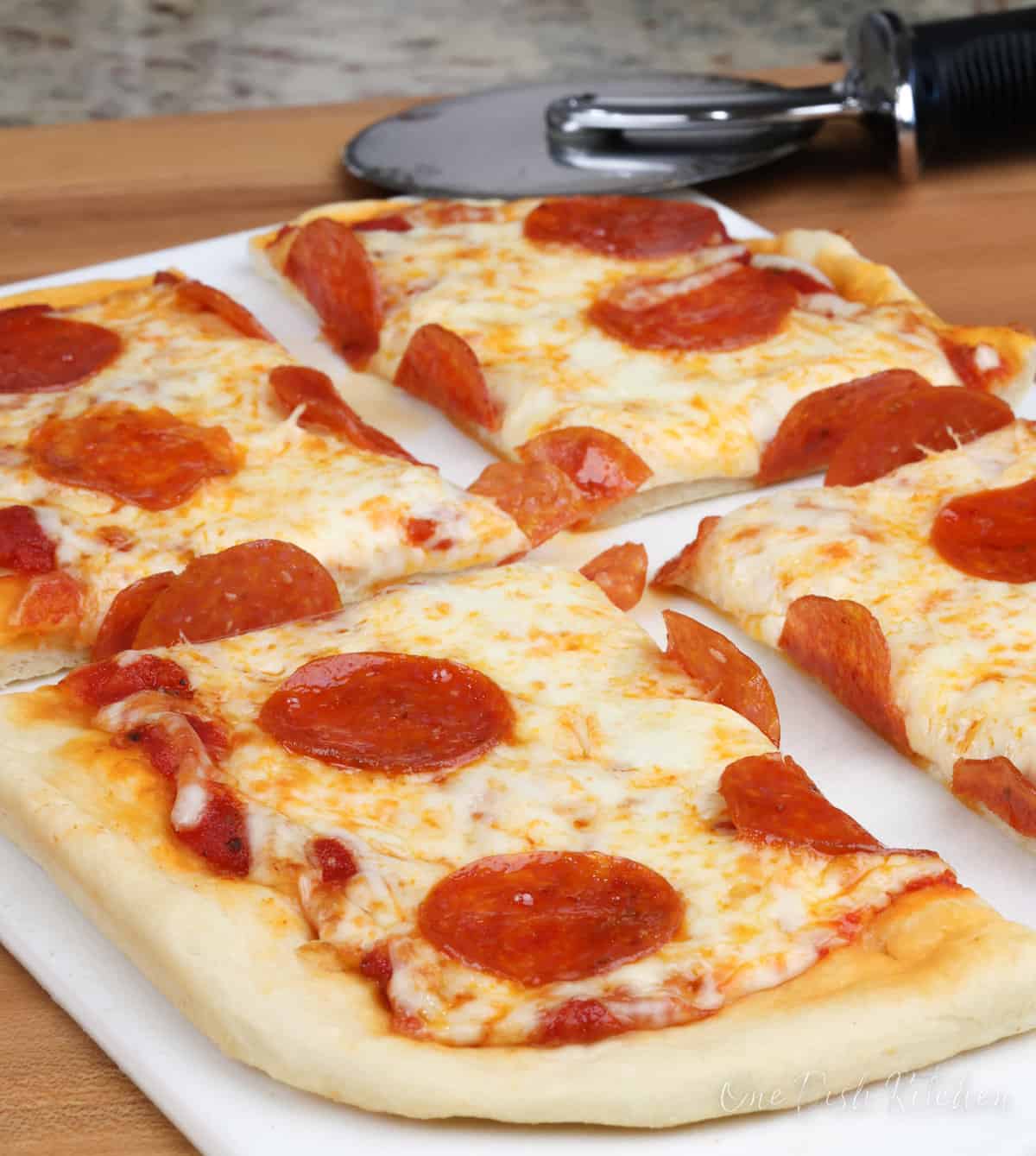 a small pepperoni pizza on a white cutting board with a pizza slicer in the background.