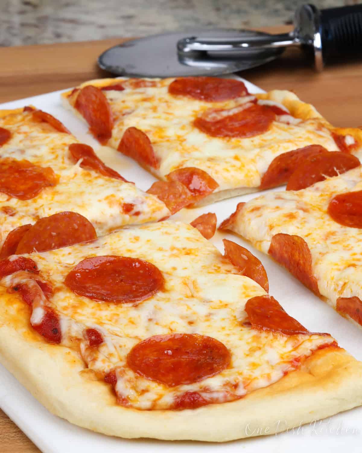 a small pepperoni pizza on a white cutting board with a pizza slicer in the background.