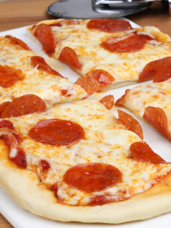 a small pepperoni pizza on a white cutting board with a pizza slicer in the background.