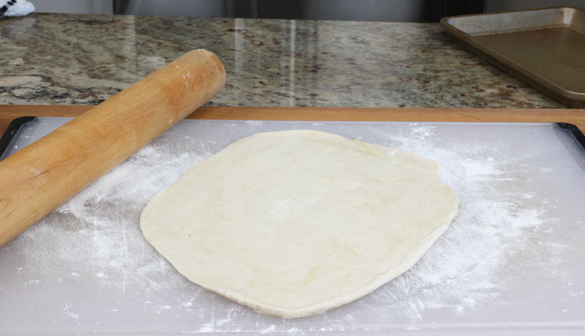 rolled out pizza dough on a white cutting board.