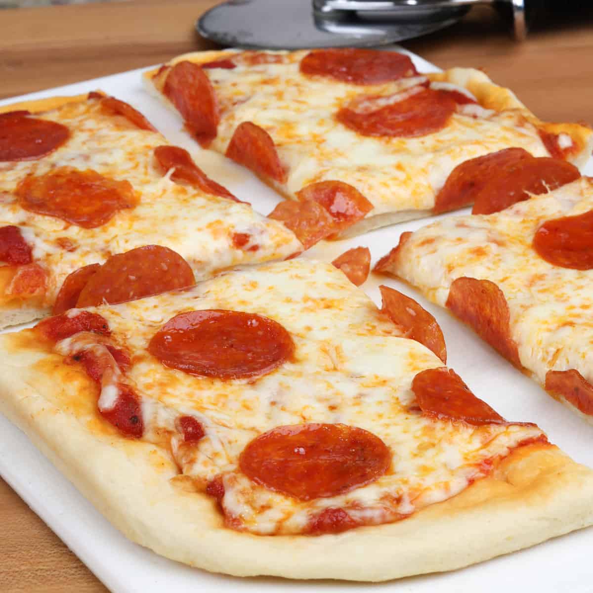 a small pepperoni pizza on a white cutting board with a pizza slicer in the background.