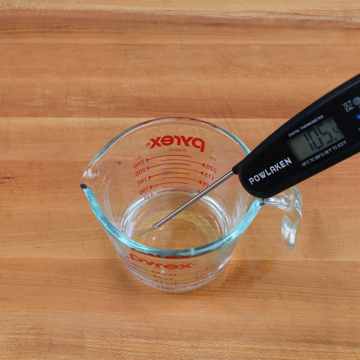 a measuring cup filled with water and an instant read thermometer in the cup measuring the temperature