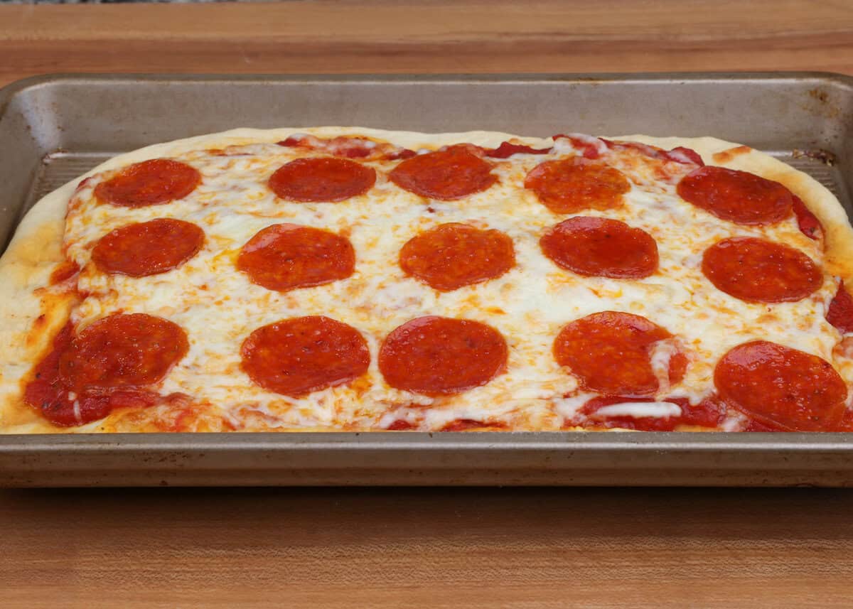 a small pepperoni pizza on a rectangular baking sheet.