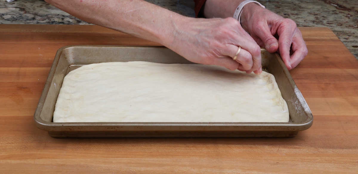 pinch the sides of pizza dough in a pan to form a crust