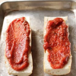 Pizza sauce spread on top of two sliced of french bread