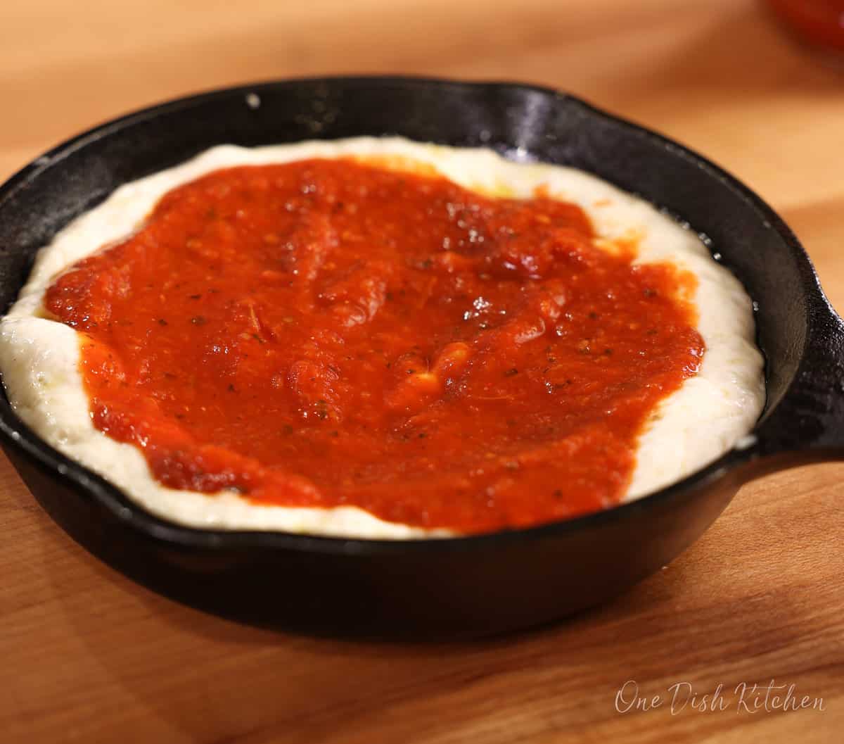 pizza sauce on pizza dough in a small cast iron skillet