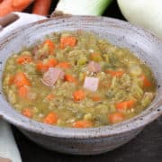 a blue bowl filled with split pea soup next to an onion, celery, and several carrots on a silver tray