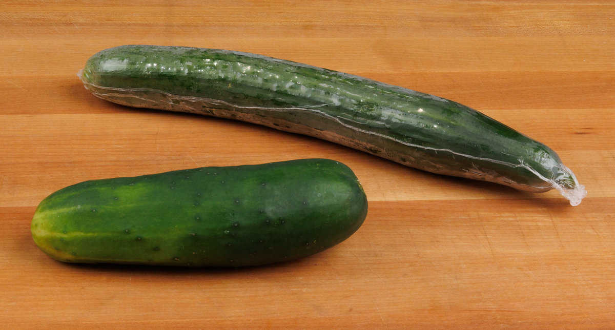 a standard cucumber next to an English cucumber on a cutting board