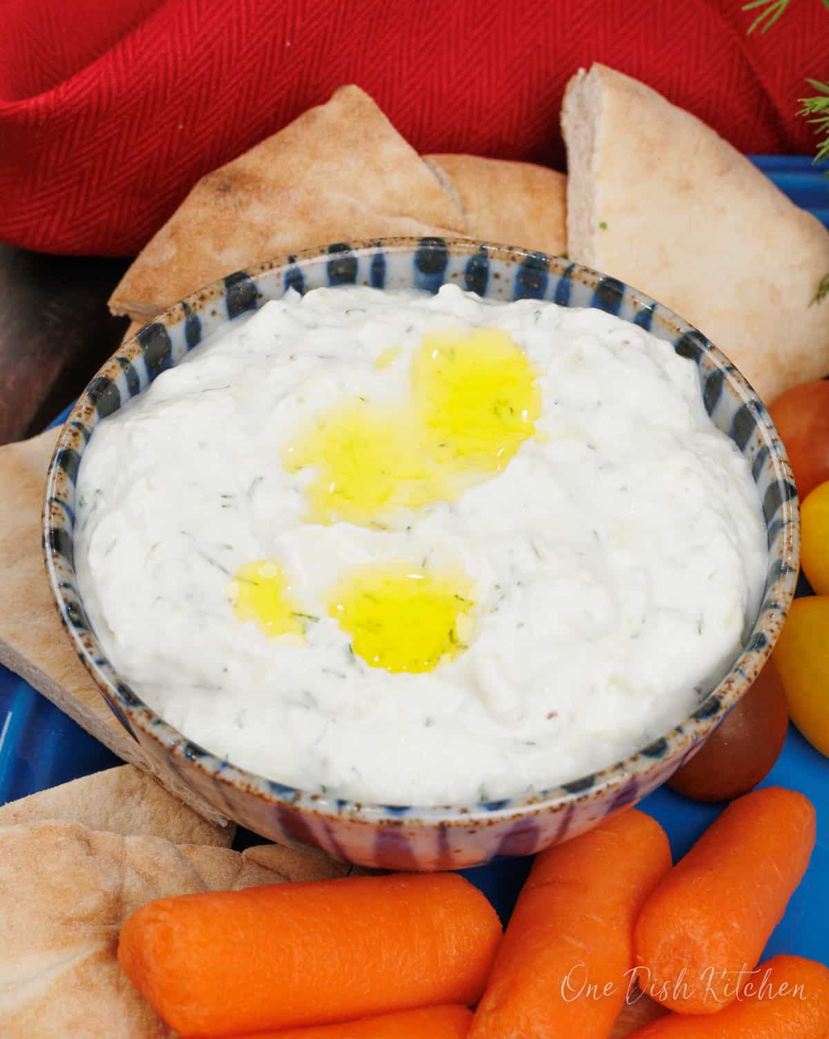 a blue bowl filled with homemade tzatziki sauce next to pita wedges and carrots