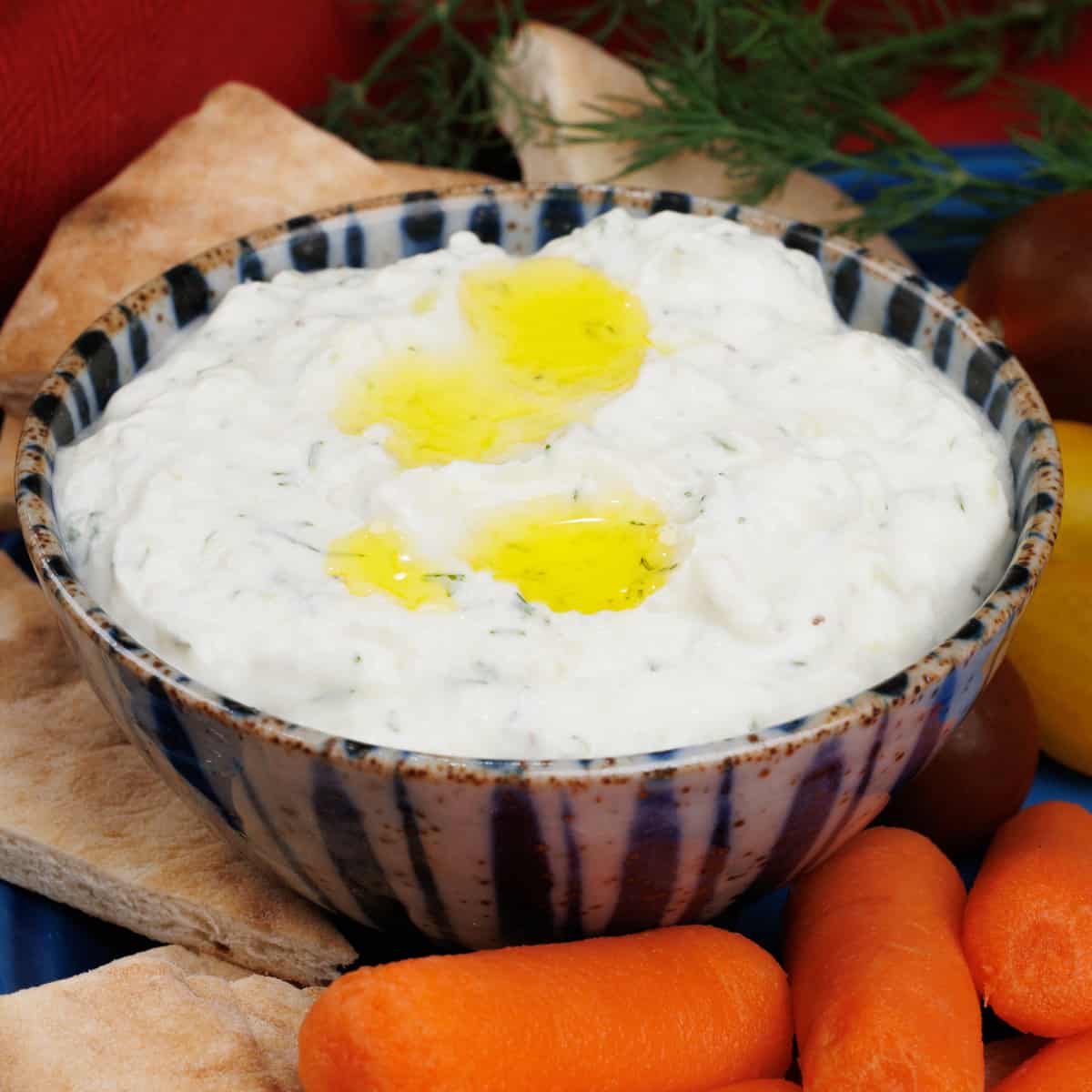tzatziki sauce topped with olive oil surrounded by pita bread, carrots, and a red napkin