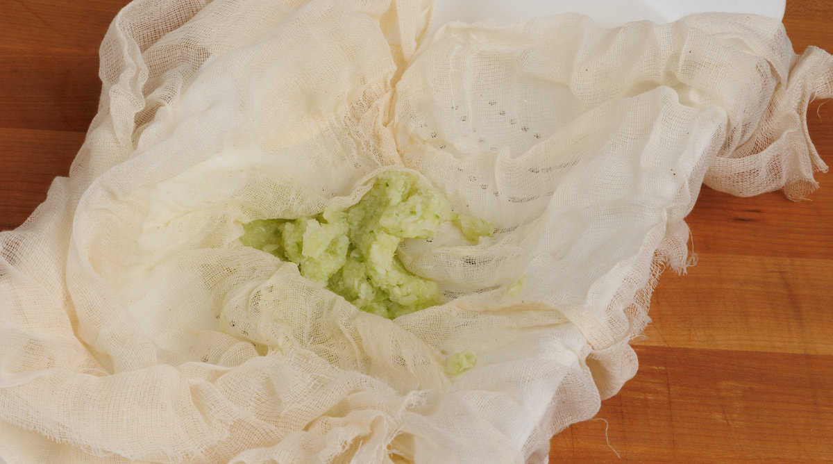 chopped cucumbers in cheesecloth over a colander releasing liquid