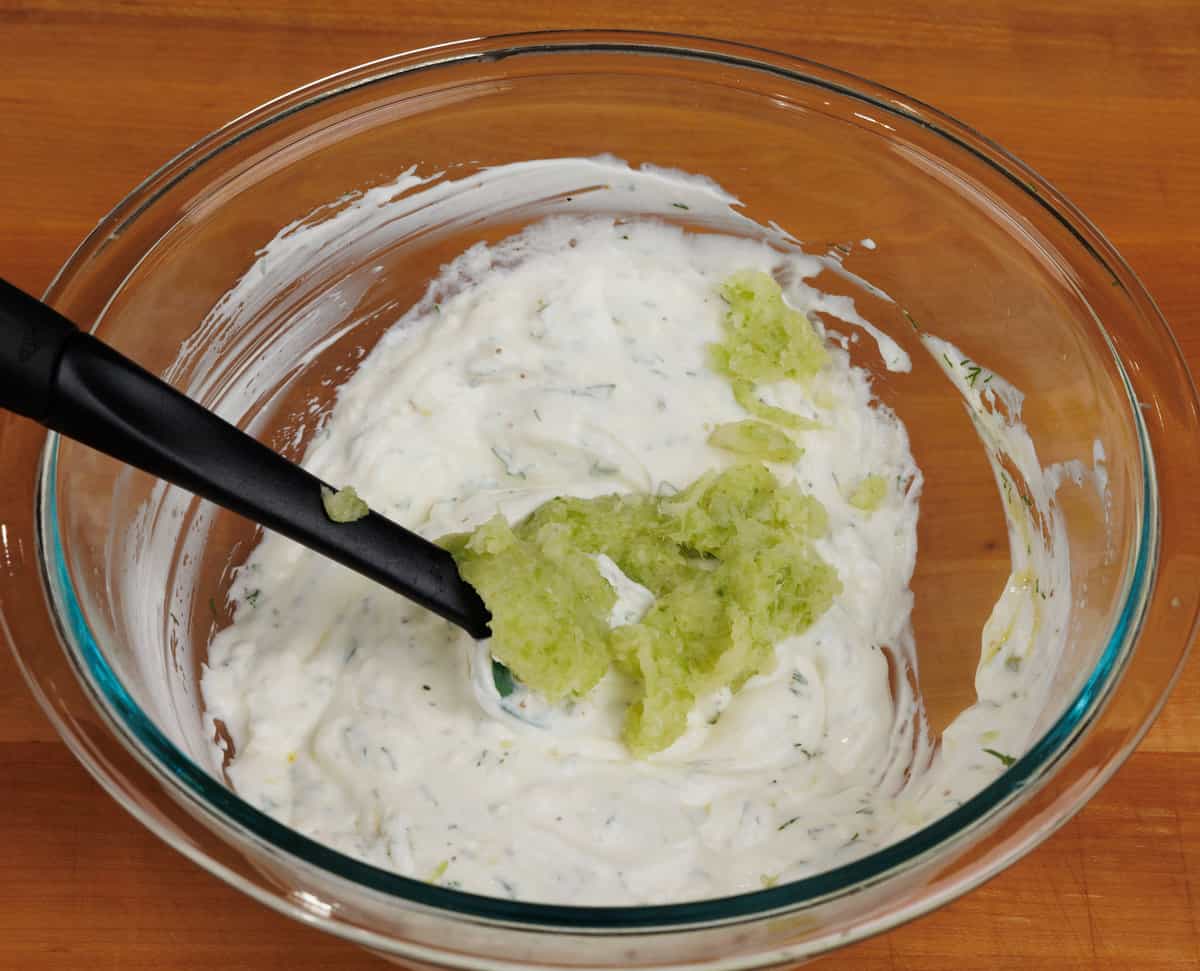 Grated cucumber stirred into greek yogurt in a mixing bowl