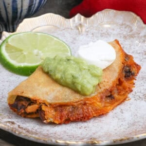 a black bean taco on a plate topped with guacamole and sour cream.