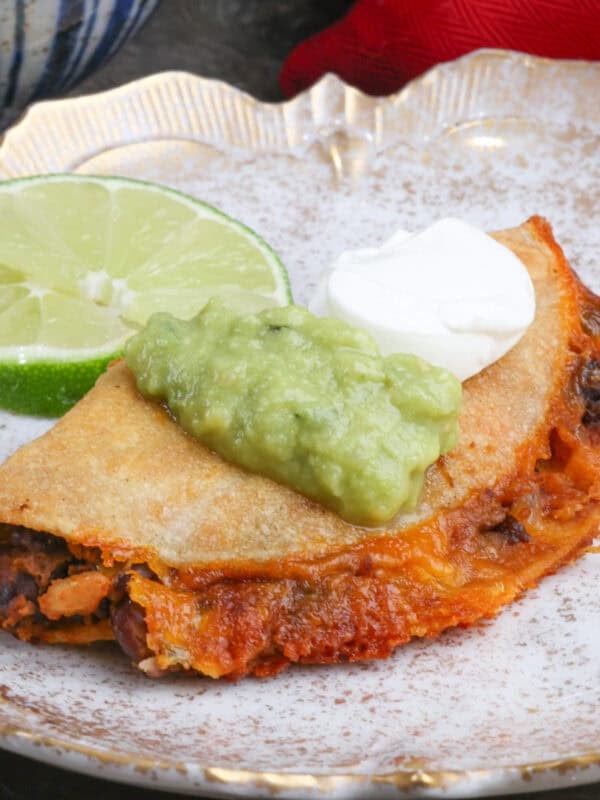 a black bean taco on a plate topped with guacamole and sour cream.