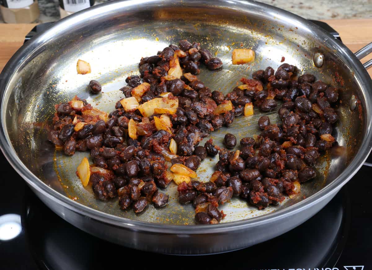 black beans, onions, and seasonings cooking in a skillet on the stove