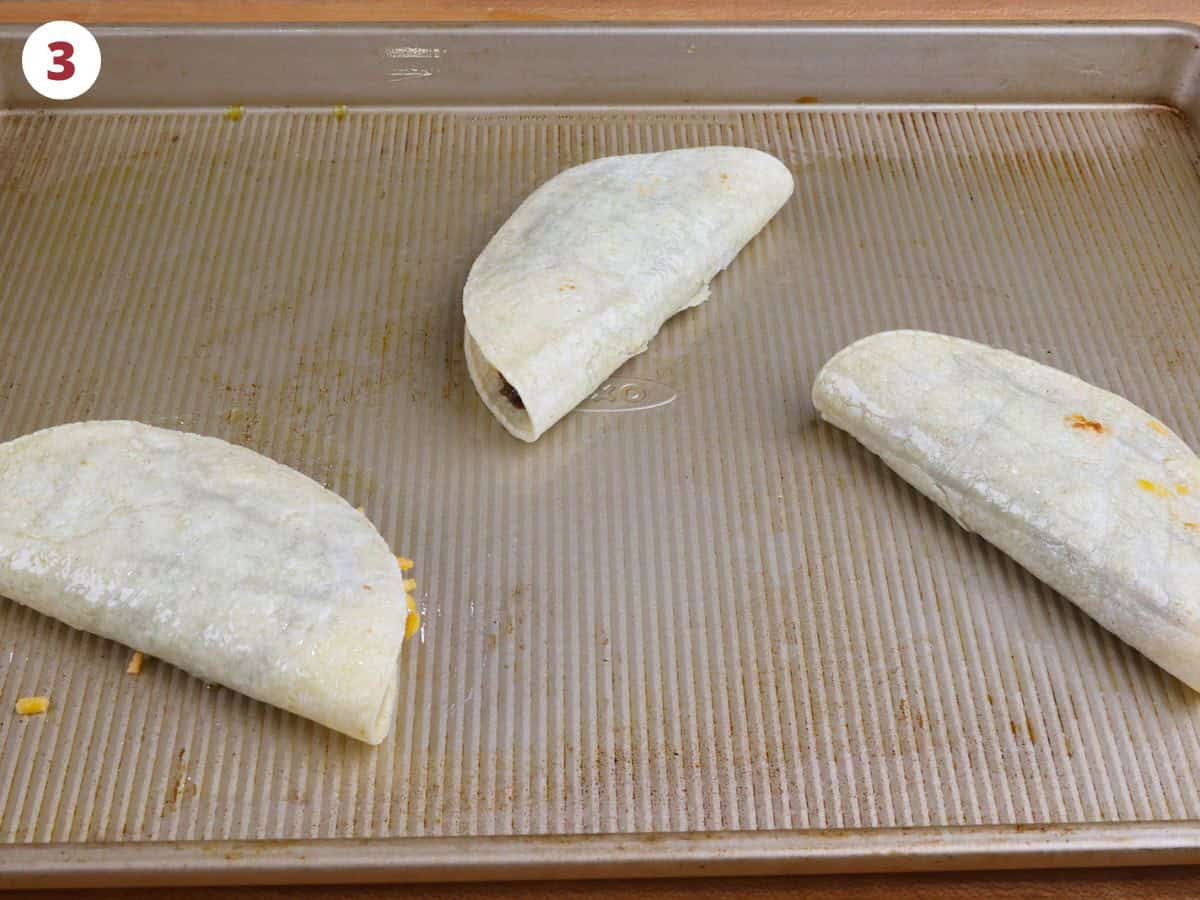 three unbaked black bean tacos on a baking sheet.