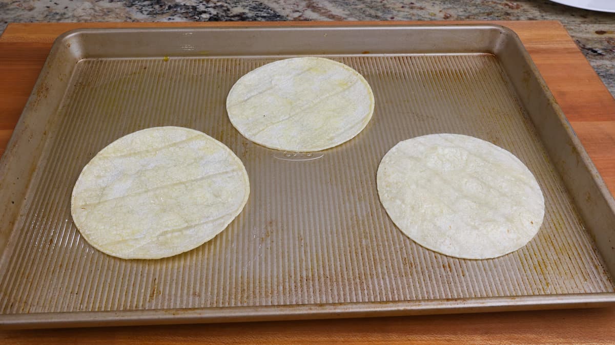 three corn tortillas on a rimmed baking sheet
