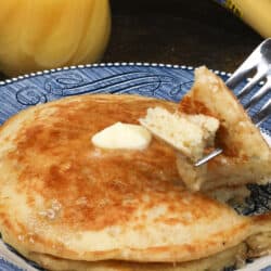 two pancakes with a fork filled with a piece of pancake on a blue plate resting on a silver tray