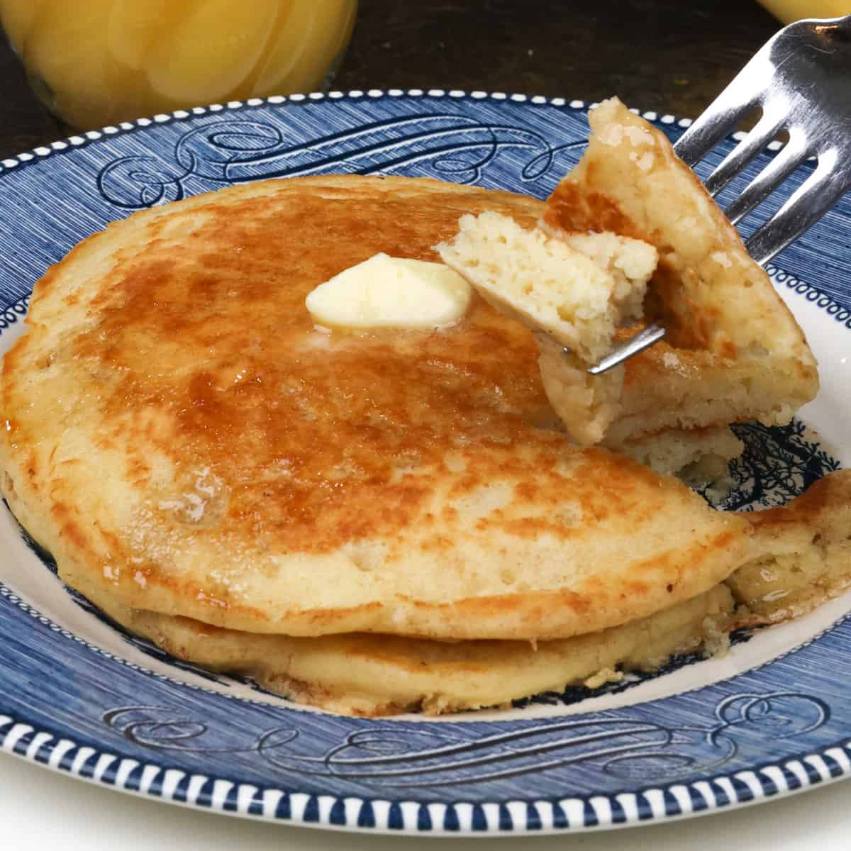 two pancakes with a fork filled with a piece of pancake on a blue plate resting on a silver tray.