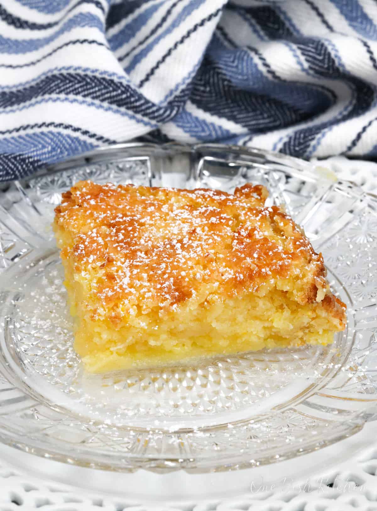 a slice of chess pie on a white plate next to a blue and white striped napkin.