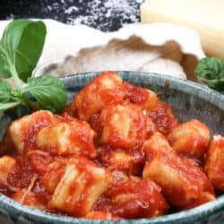 potato gnocchi topped with tomato sauce in a green bowl next to fresh basil and parmesan cheese