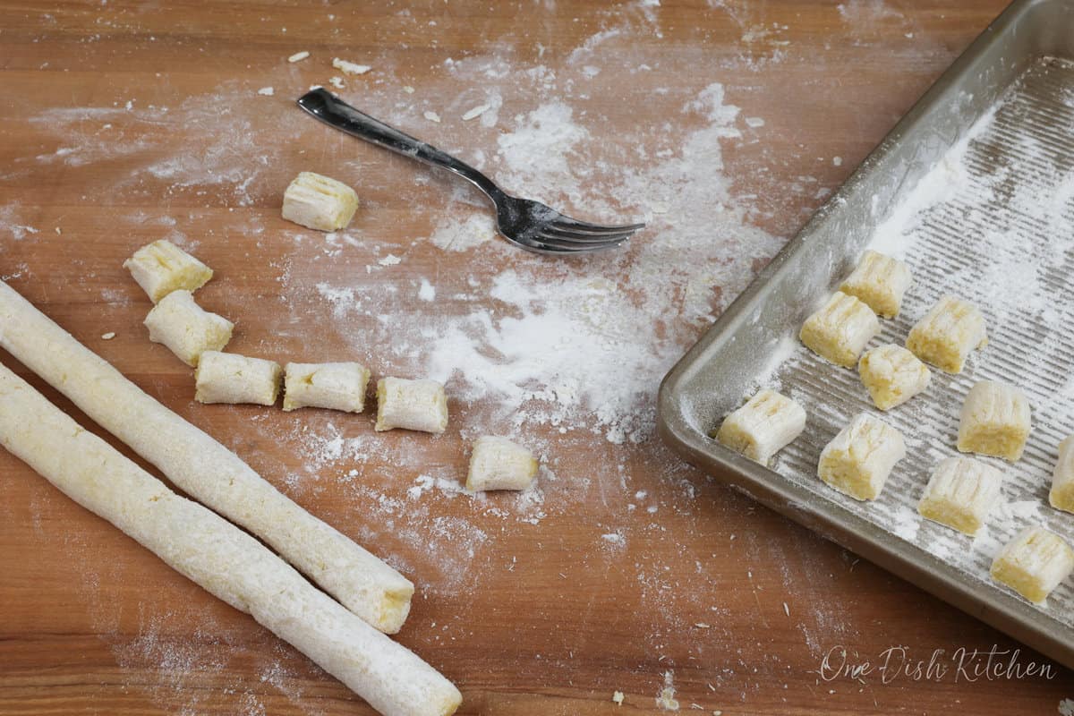 uncooked potato gnocchi on a floured cutting board next to a fork.