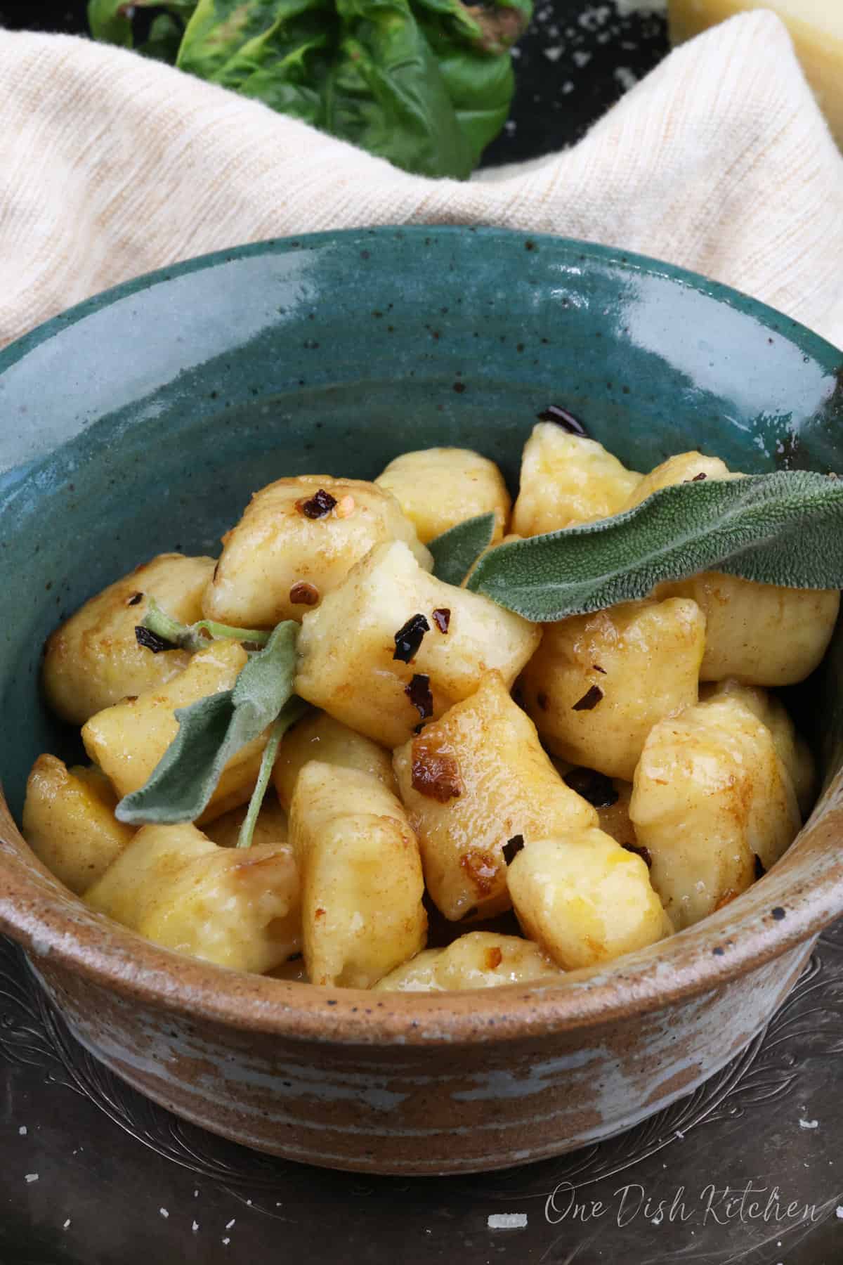gnocchi with butter and sage in a green bowl next to a brown napkin