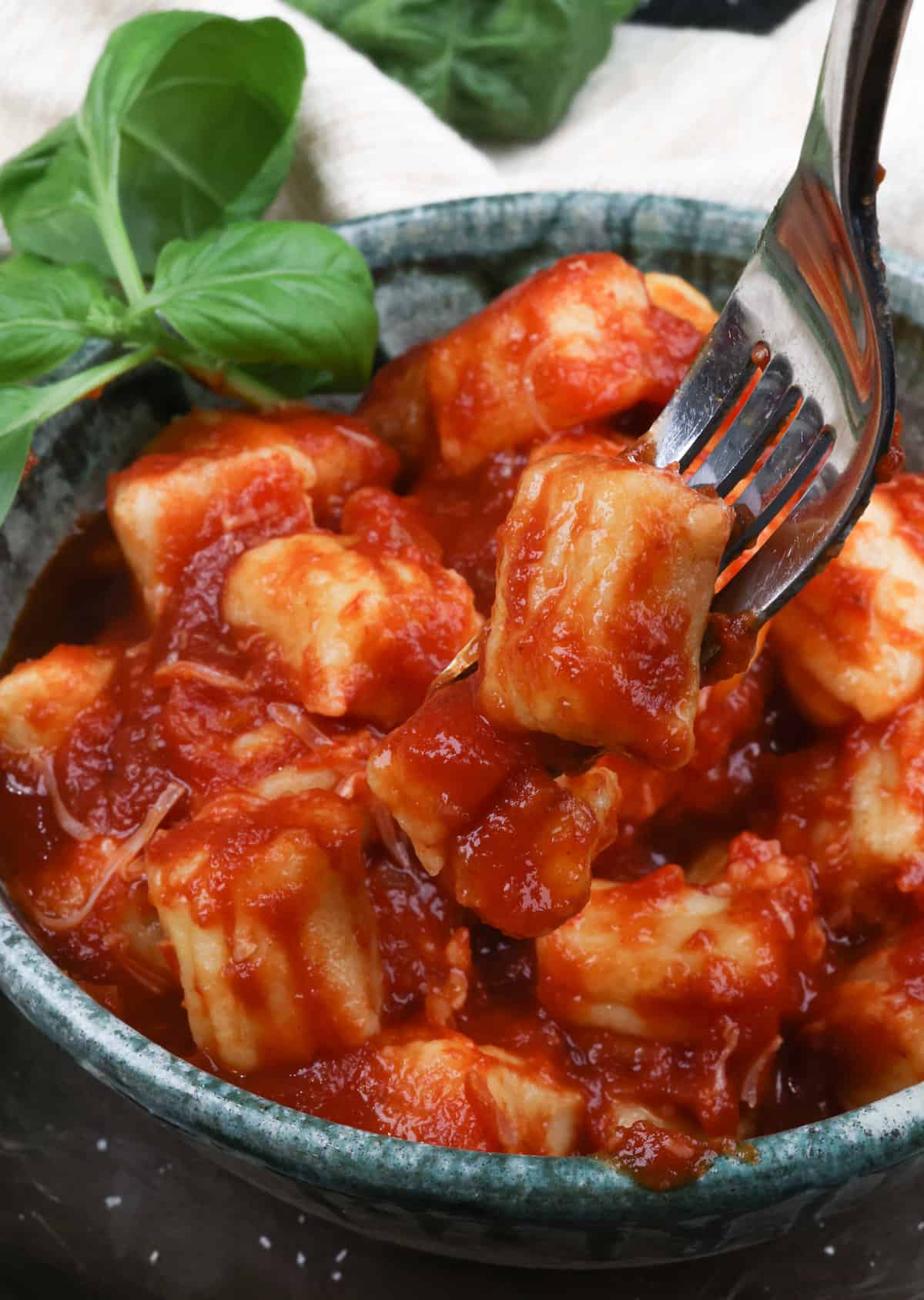 potato gnocchi on a fork above a green bowl filled with additional gnocchi topped with tomato sauce.