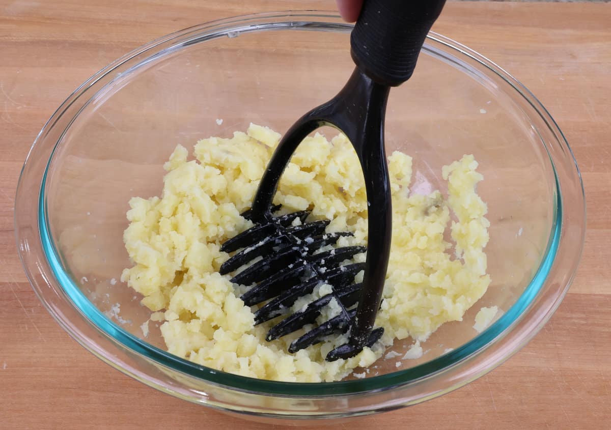 potatoes in a bowl mashed with a potato masher
