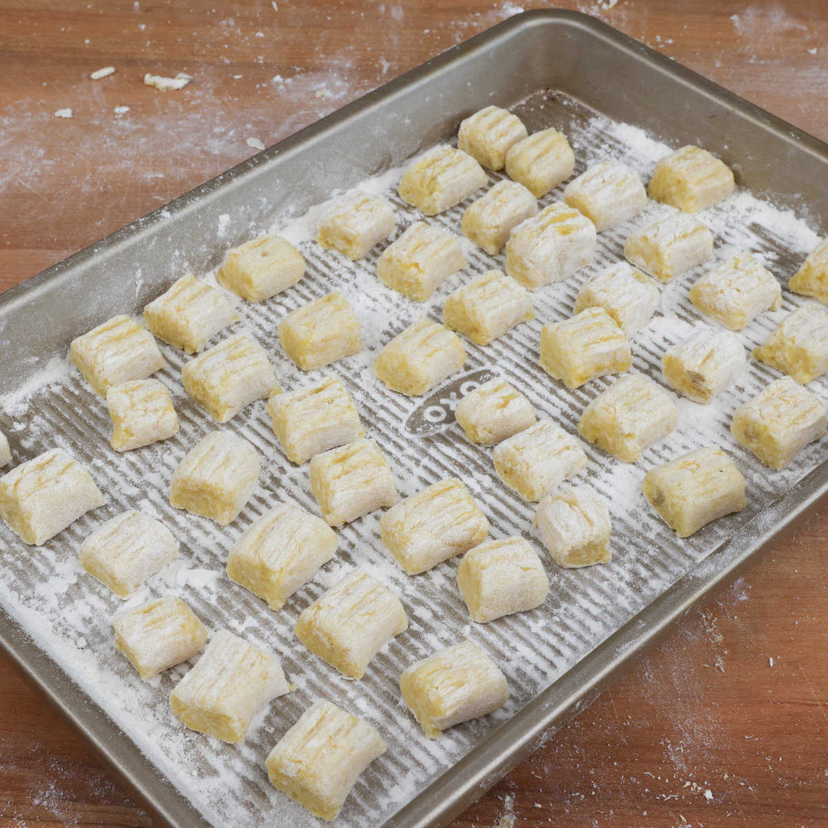 a rimmed baking sheet filled with uncooked potato gnocchi lightly dusted with flour