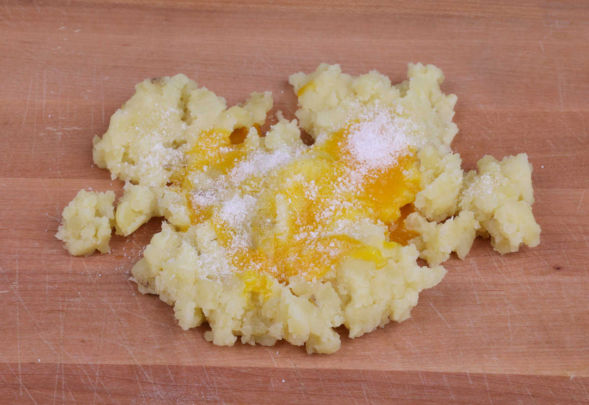 mashed potatoes topped with egg yolk and salt on a cutting board.